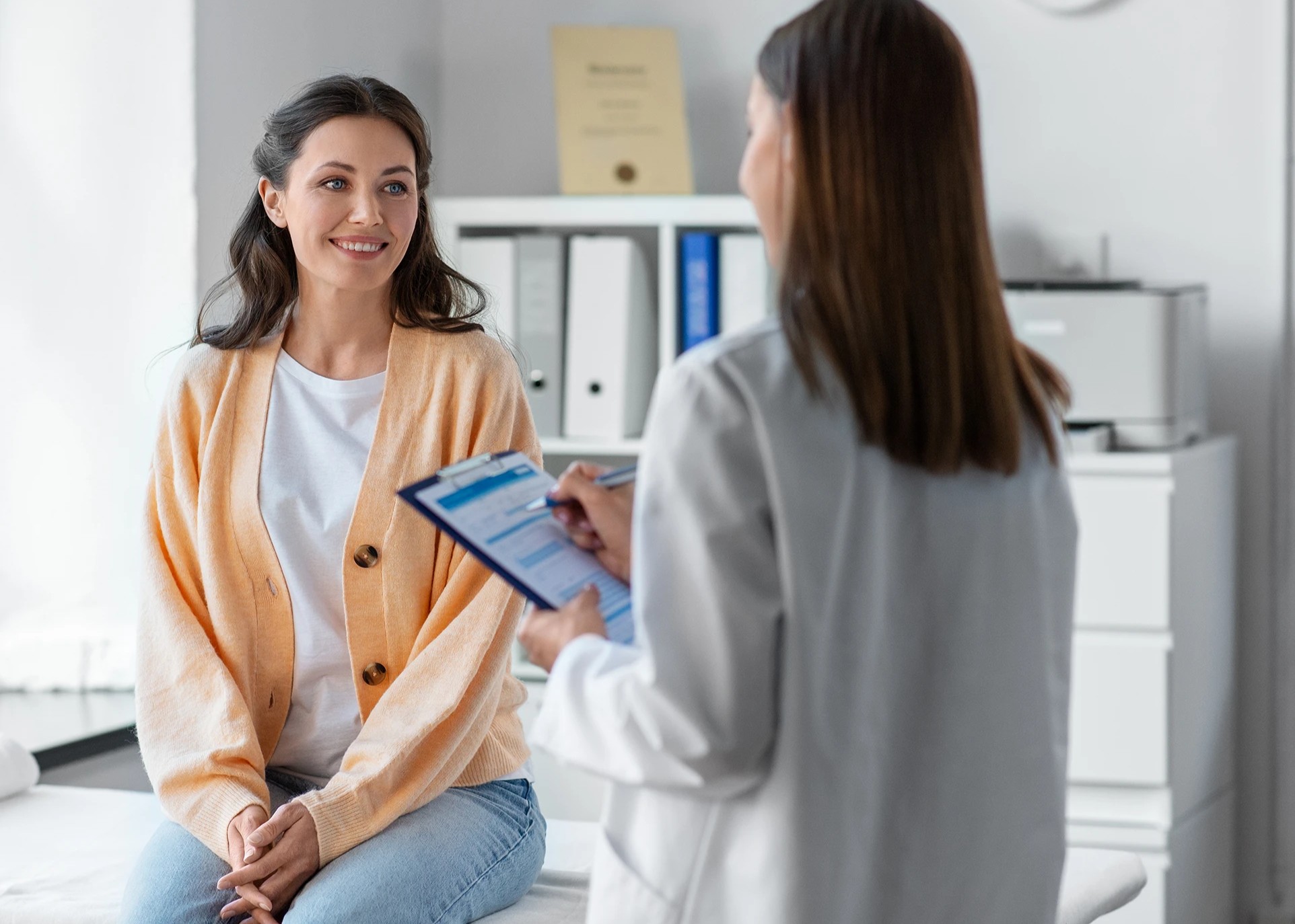Smiling woman in peach sweater sits on exam table during family medicine appointment